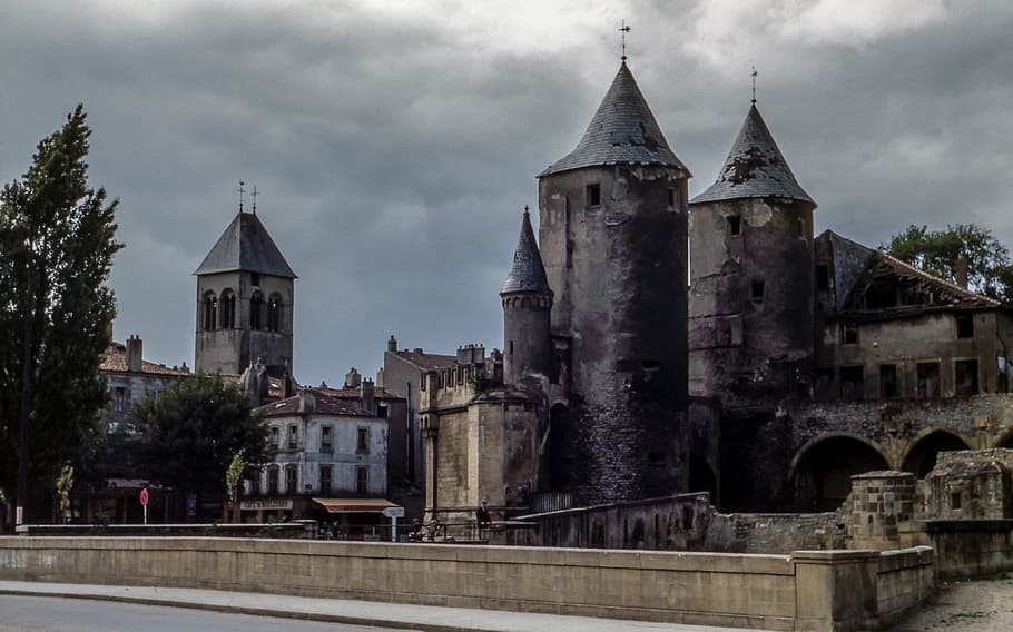 photo of gray an brown structure during cloudy day, trees near castle under dark cloudy sky