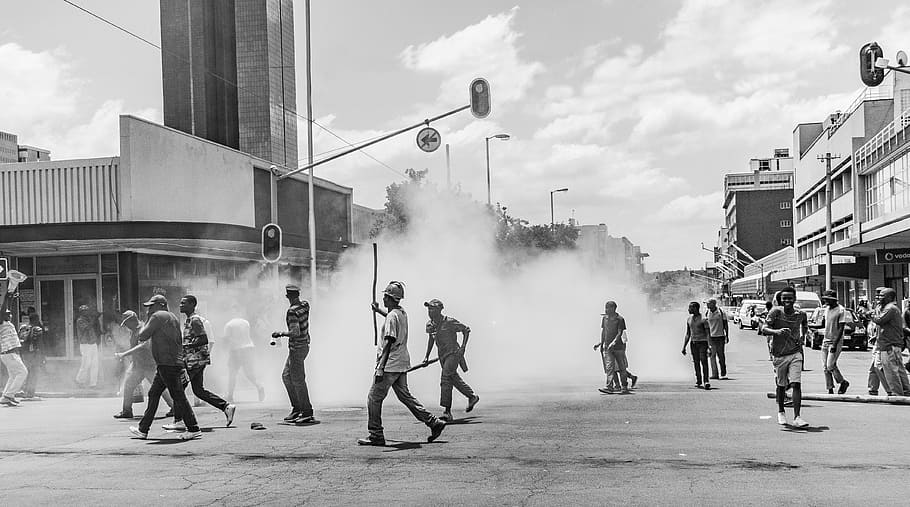 grayscale photo of people on street near buildings during daytime, crowd of people running on concrete road near smoke screen