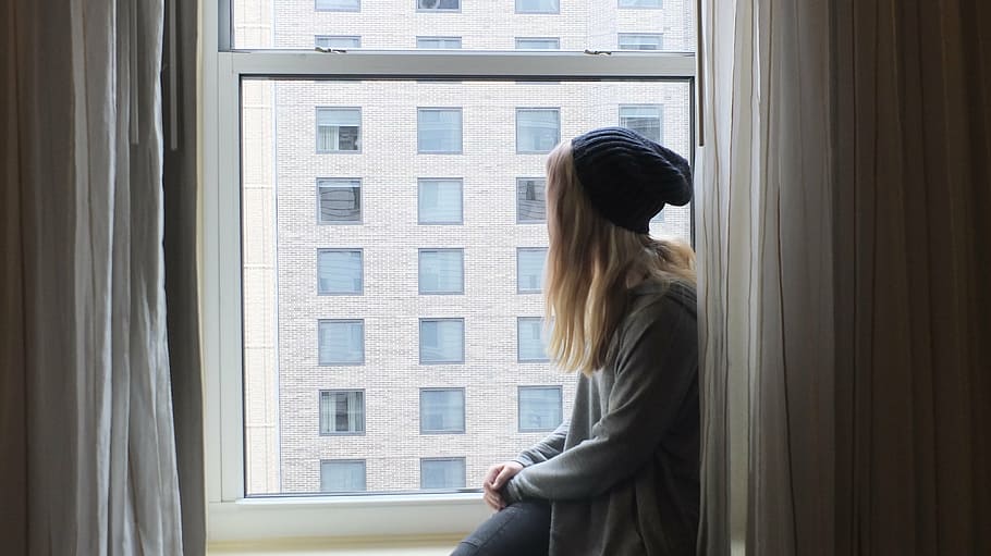 woman wearing knit hat sitting on window, gaze, think, thinker