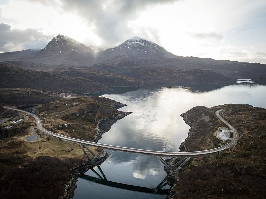 concrete road bridge near two snow-capped mountains during daytime, aerial photography of road between lake HD wallpaper