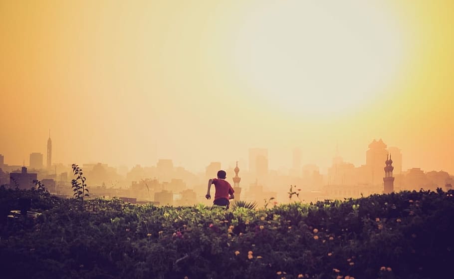 man running towards the city on green grass field during golden time, Boy running in field HD wallpaper