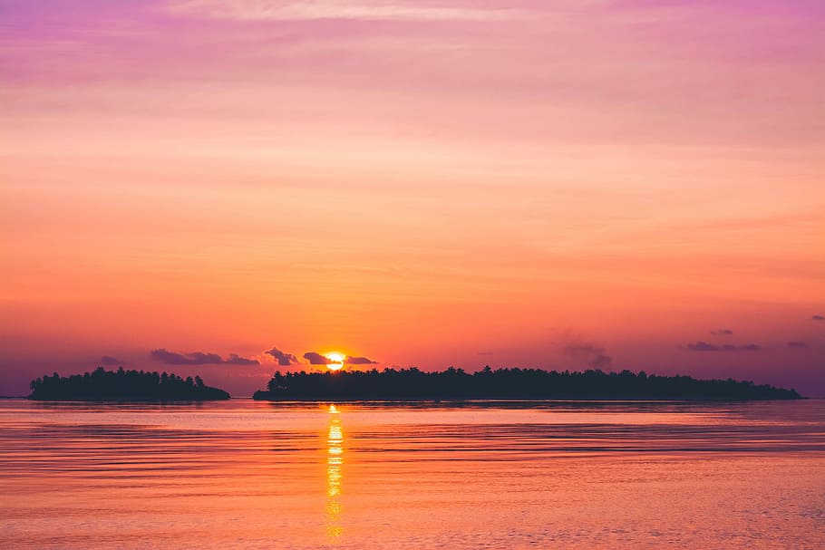 sunset over horizon, two island surrounding calm body of water during golden hour HD wallpaper