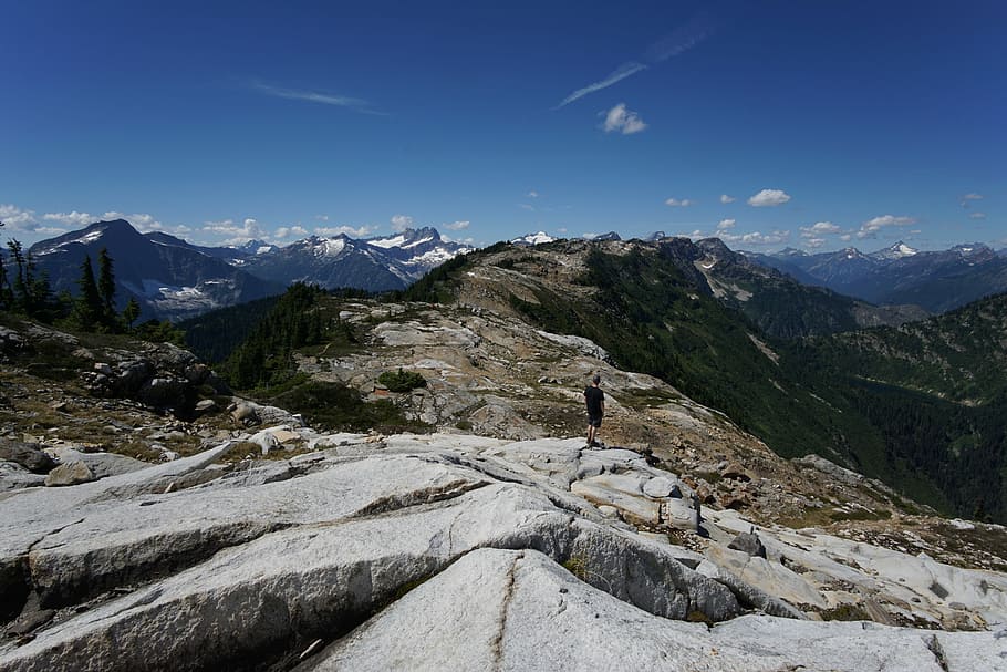 person standing on rock facing mountains during daytime, man standing on rocky mountain during daytime HD wallpaper