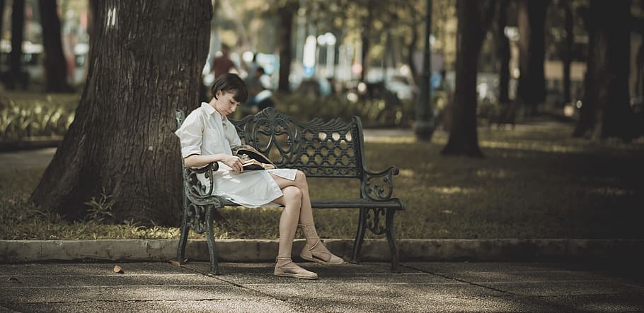 Woman Sitting on Metal Bench on Park While Reading Book, blurred background