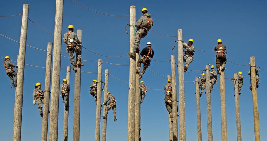 group of men wearing gray and black coveralls climbing electrical post during daytime HD wallpaper
