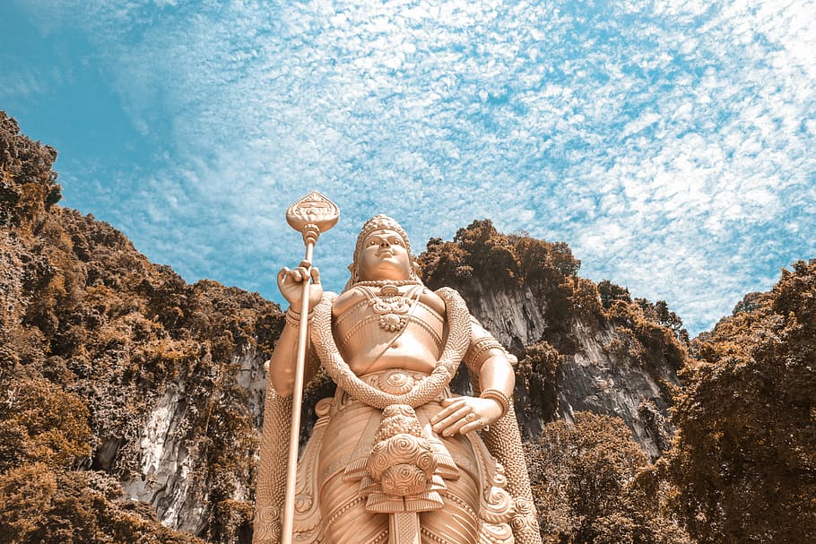statue of Lord Shiva, gold-colored Buddha statue with brown mountain in background under blue sky during daytime