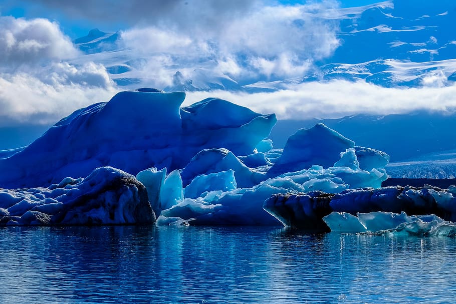 iceberg beside cliff under cloudy sky during daytime, blue ice formation under white skies HD wallpaper