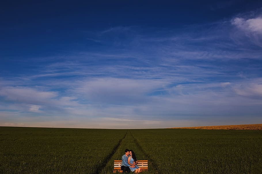 photo of two man and woman sitting on bench on grass field, man and woman sitting on bench surrounded by grass HD wallpaper