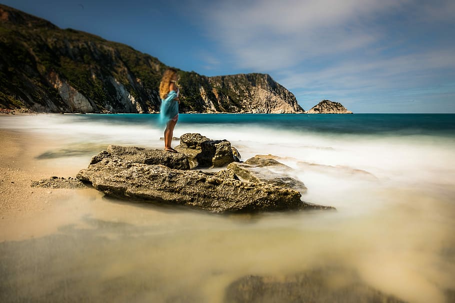 woman standing on rock at beach during daytime, woman in blue shirt standing on top of gray stone beside body ofwater HD wallpaper