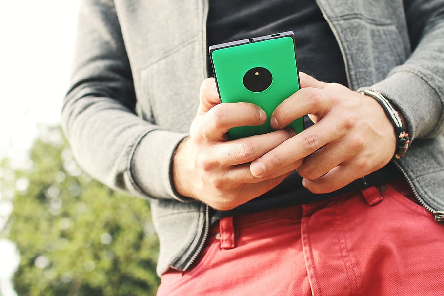 man wearing gray jacket and red bottoms holding smartphone HD wallpaper
