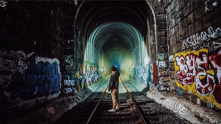 man standing in middle of train track tunnel, train tracks, graffiti