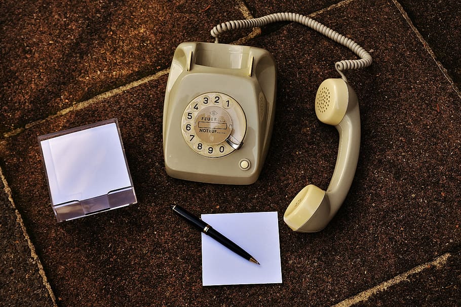 beige rotary telephone beside white paper and retractable pen