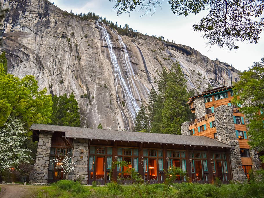 building in the foot of the mountain near trees, waterfalls behind building surrounded by trees HD wallpaper