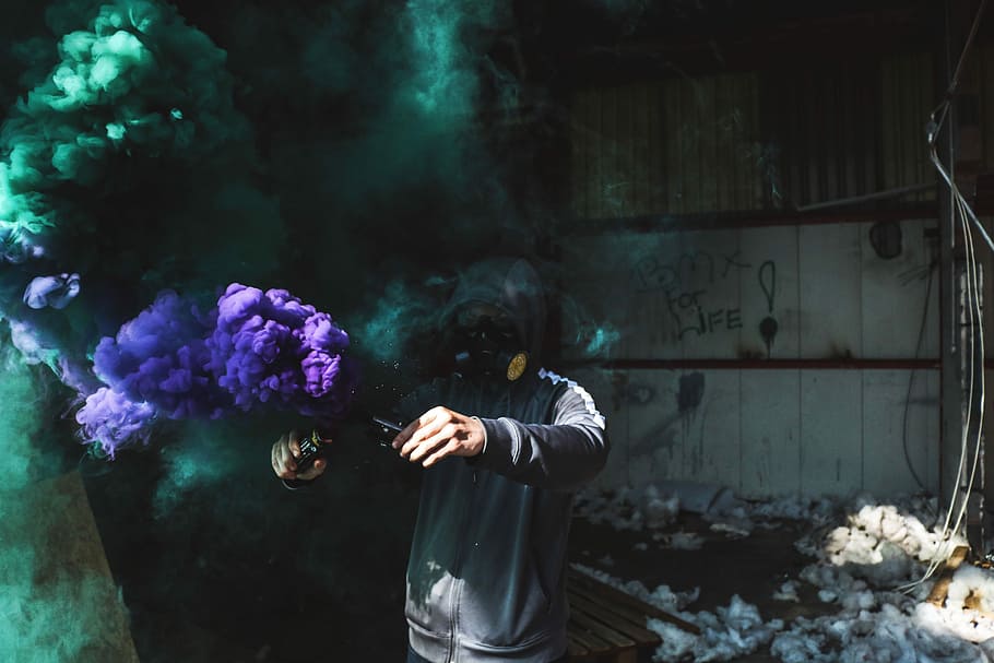 man in black jacket, person using purple and green smoke bomb