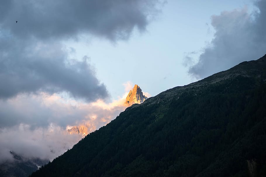 sun lighting summit of brown mountain showing on side of the mountain, mountain covered with forest HD wallpaper