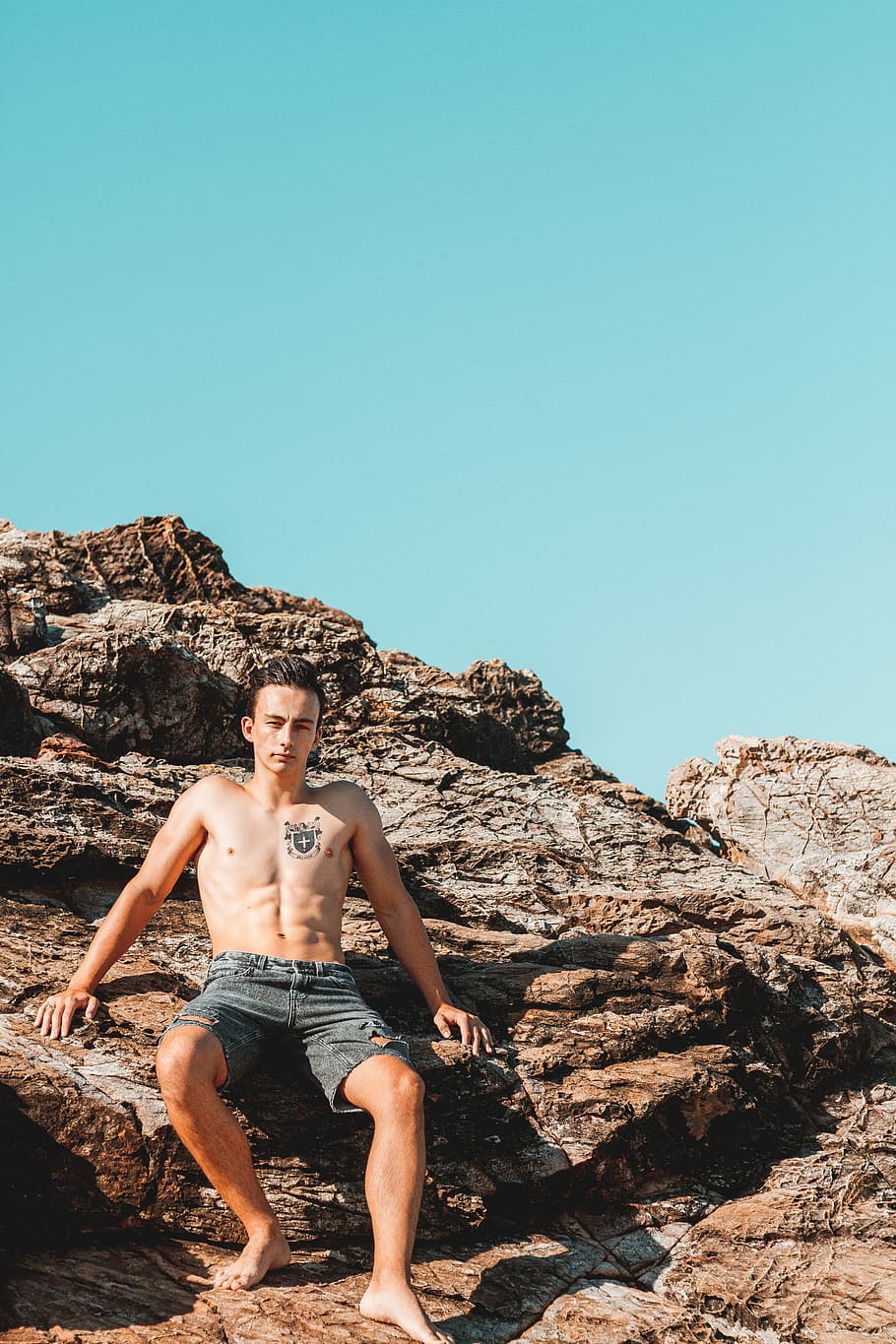 man sitting on rock fragment during daytime, man in black denim shorts sitting on rock formation HD wallpaper
