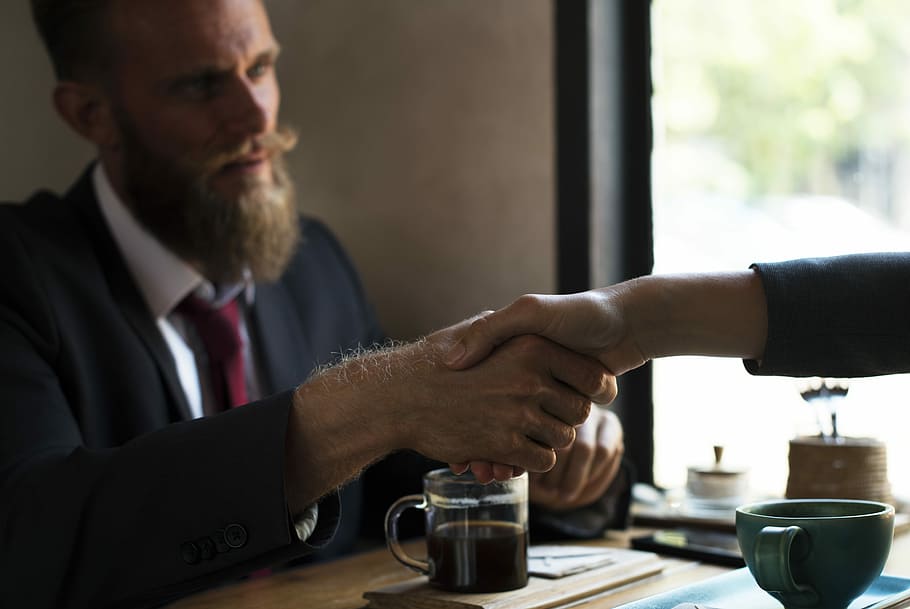 man in black suit seated in front of table while shaking the hand of person in black blazer HD wallpaper