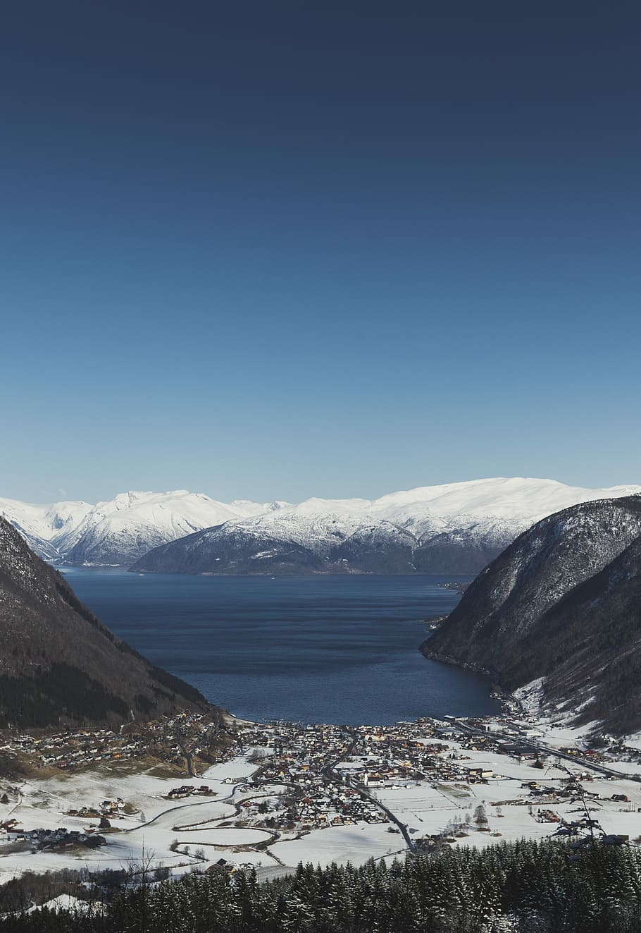 city near the ocean during winter, aerial photography of mountain range beside sea under clear blue sky HD wallpaper