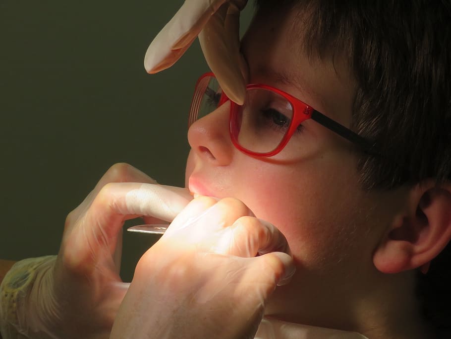 dentist checks teeth of boy with red eyeglasses, dental braces