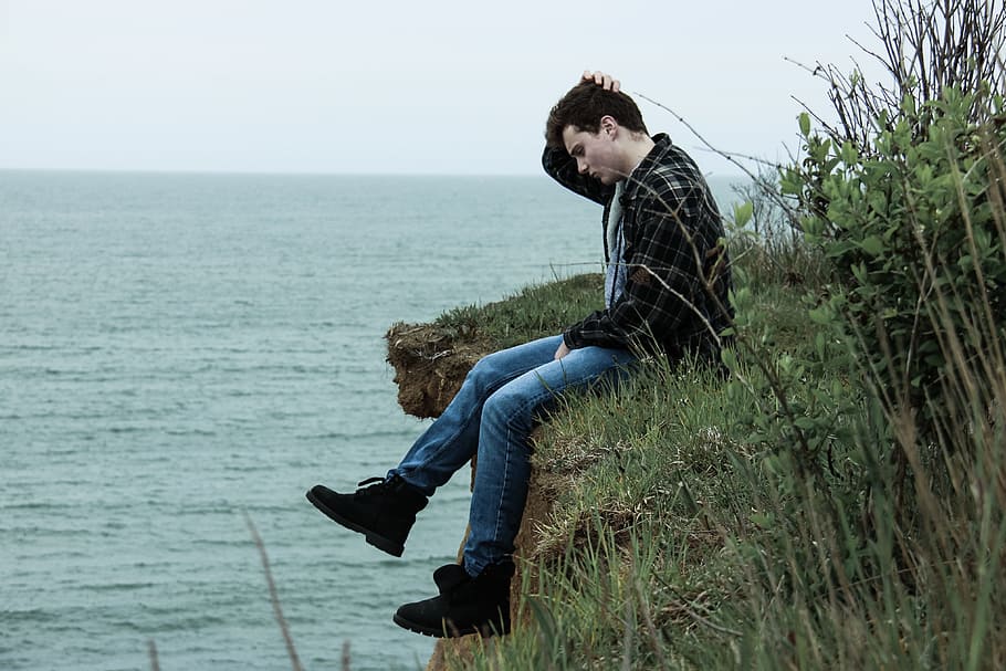 man sitting in the edge of mountain surrounded by grass, ocean HD wallpaper
