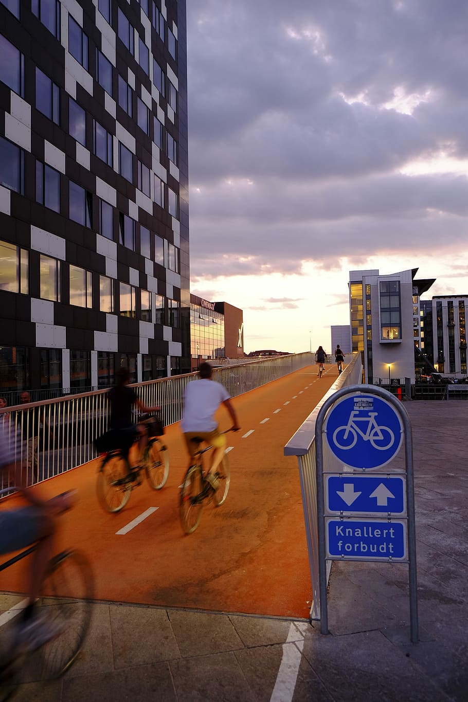 people riding bicycles inside bicycle lane beside skyscraper, two person riding bicycle near grey concrete building under cloudy sky HD wallpaper