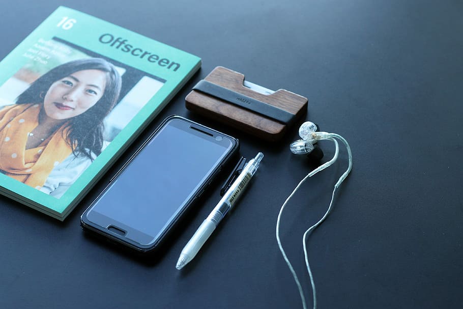 black Android smartphone beside white earbuds, white click pen, and Offscreen book, OFF SCreen case beside black Android smartphone and click pen on black surface HD wallpaper
