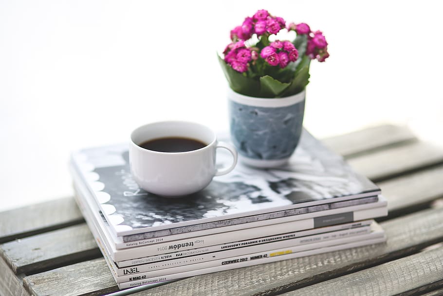 cup of coffee on stack of books, newspaper, magazine, flower