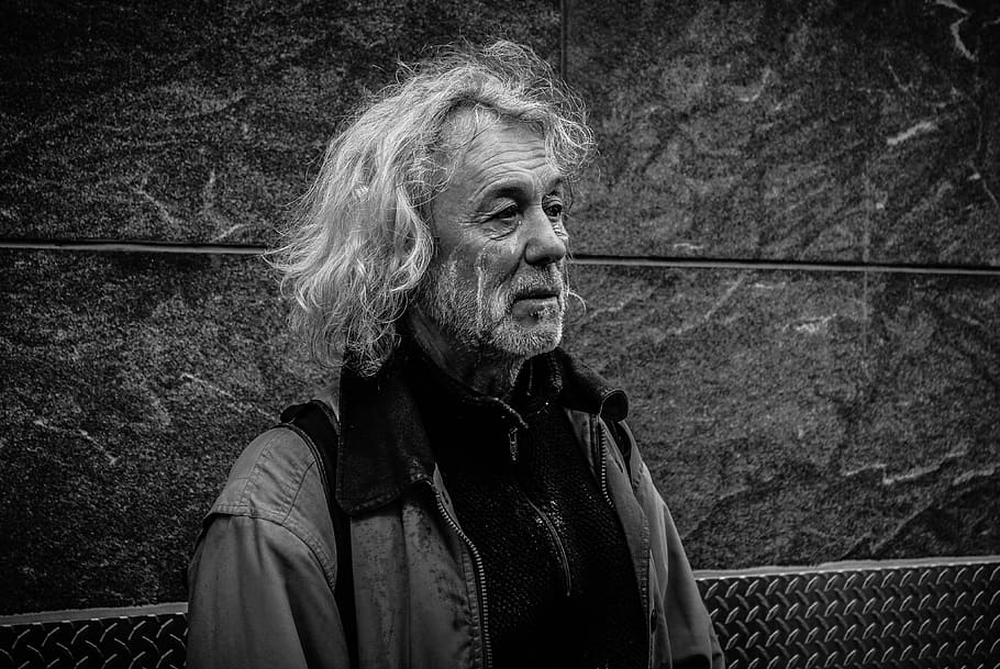 grayscale photo of long-haired man, man standing near grey wall outdoors HD wallpaper