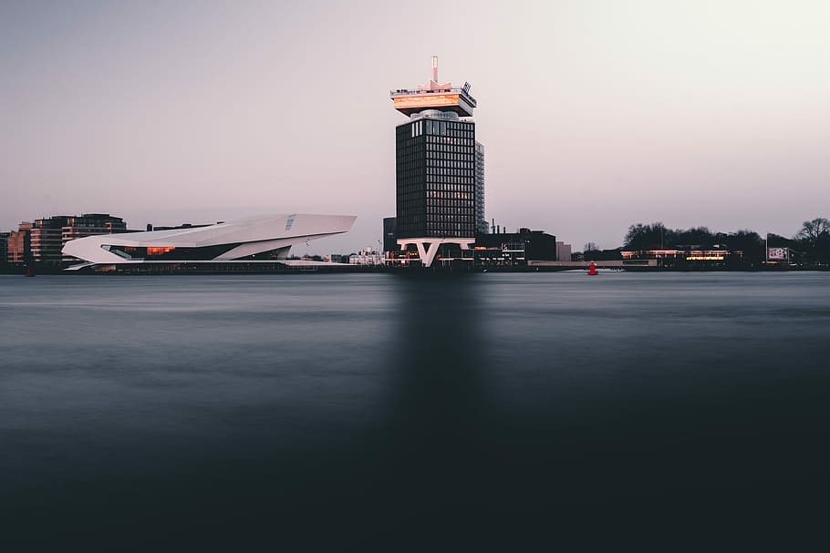 Burning reflecting sunset, gray curtain building near calm body of water during daytime HD wallpaper