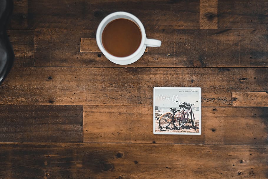 White Ceramic Mug With Coffee Beside Photo of Two Mountain Bikes HD wallpaper