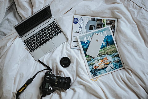 Silver laptop, a camera, magazines and other items on white bed sheets HD wallpaper