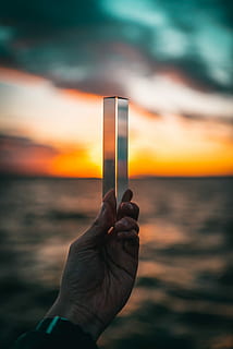 person holding gray metal case outdoors, person holding clear glass against the horizon during sunset HD wallpaper