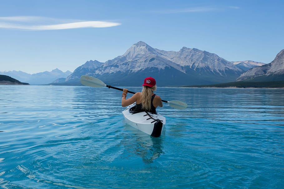 woman kayaking in calm body of water with mountain alps in distance during daytime HD wallpaper