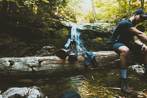 man sitting on tree log beside boots, man sitting on tree trunk lying on river at daytime HD wallpaper