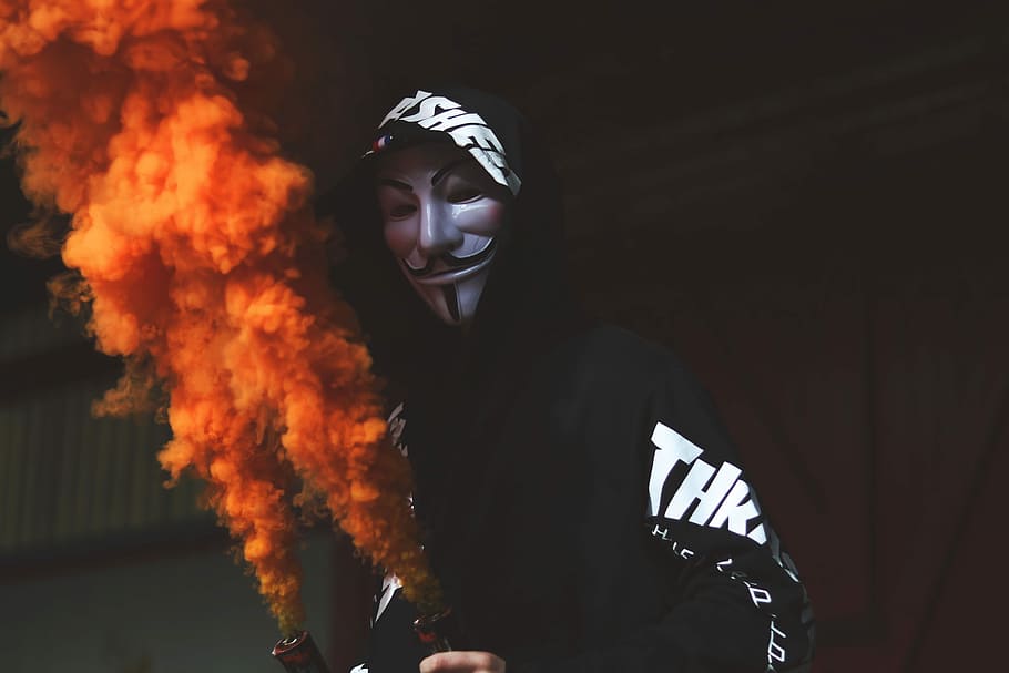 person wearing guy fawkes mask, person wearing Guy Fawkes mask opening pump with orange smoke
