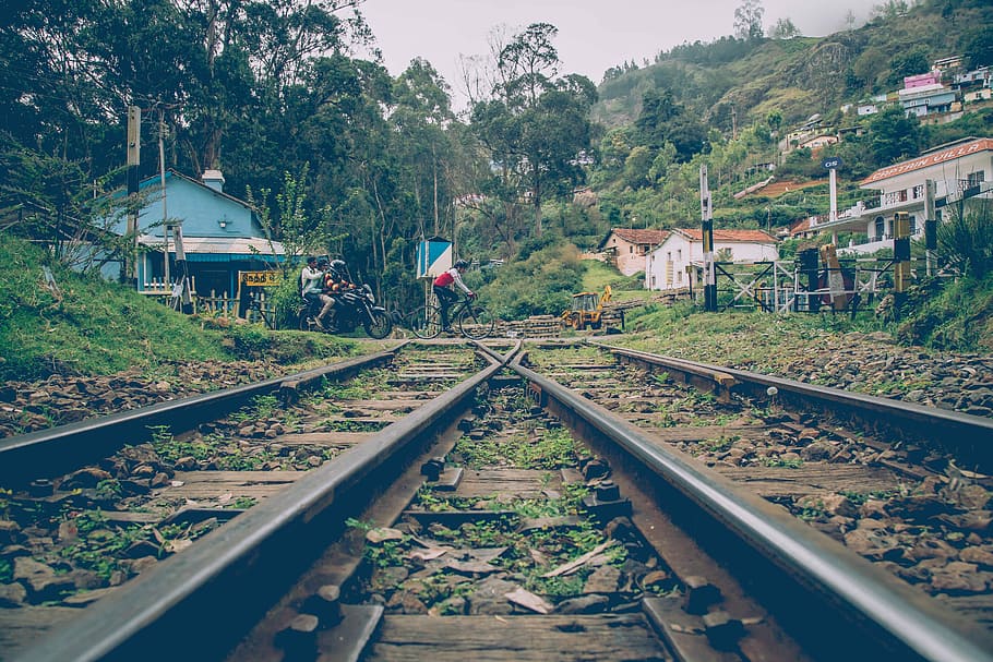 two person riding motorcycle crossing on railroad during daytime, black metal train trail near white and blue concrete houses HD wallpaper