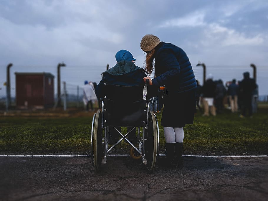 woman standing near person in wheelchair near green grass field, person on wheelchair in front of grass