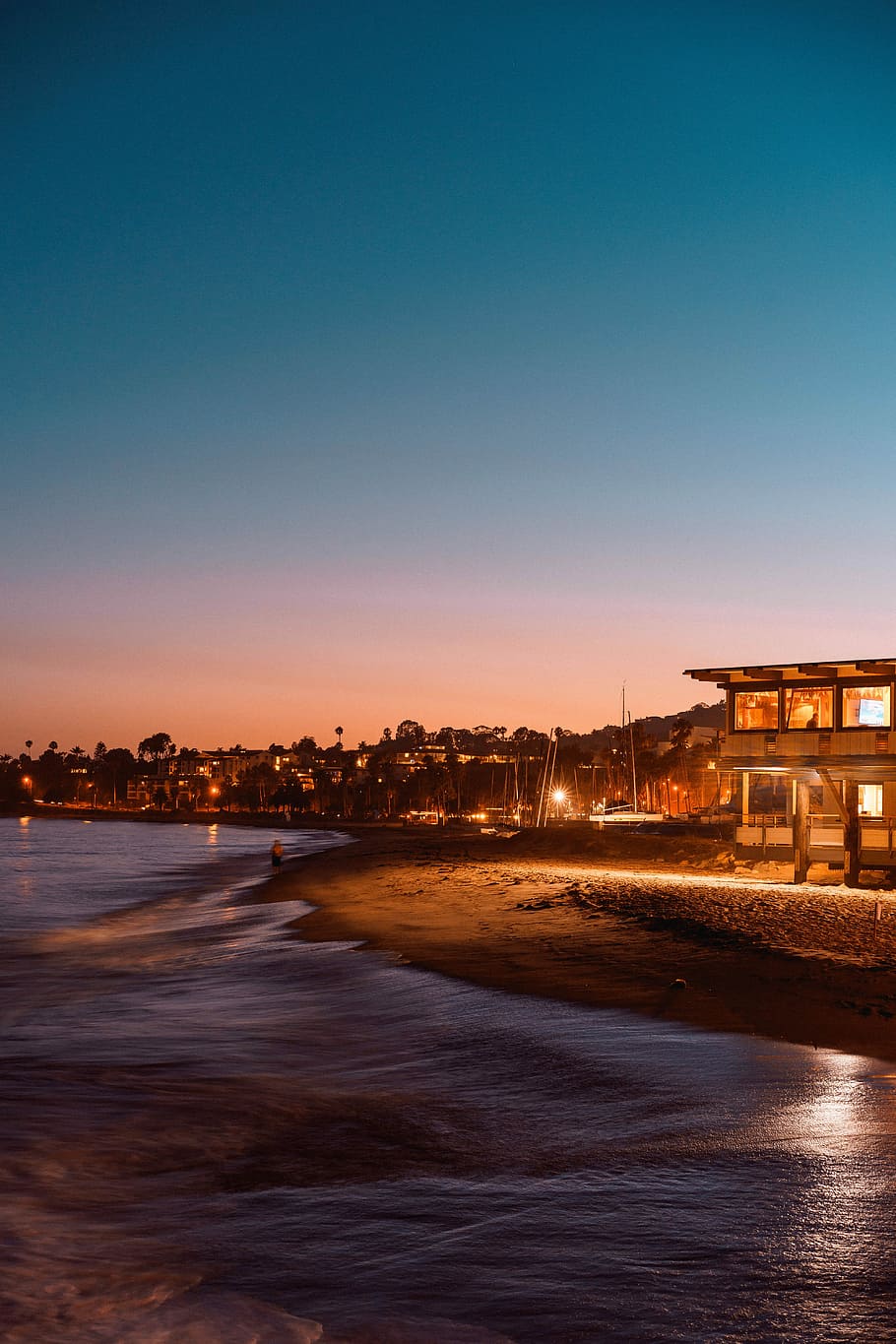 house beside body of water, person walking on the beach in distant of buildings HD wallpaper