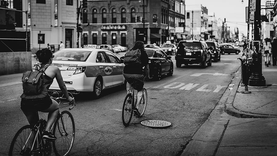 greyscale photo of people in bike riding along cars on road with buildings HD wallpaper