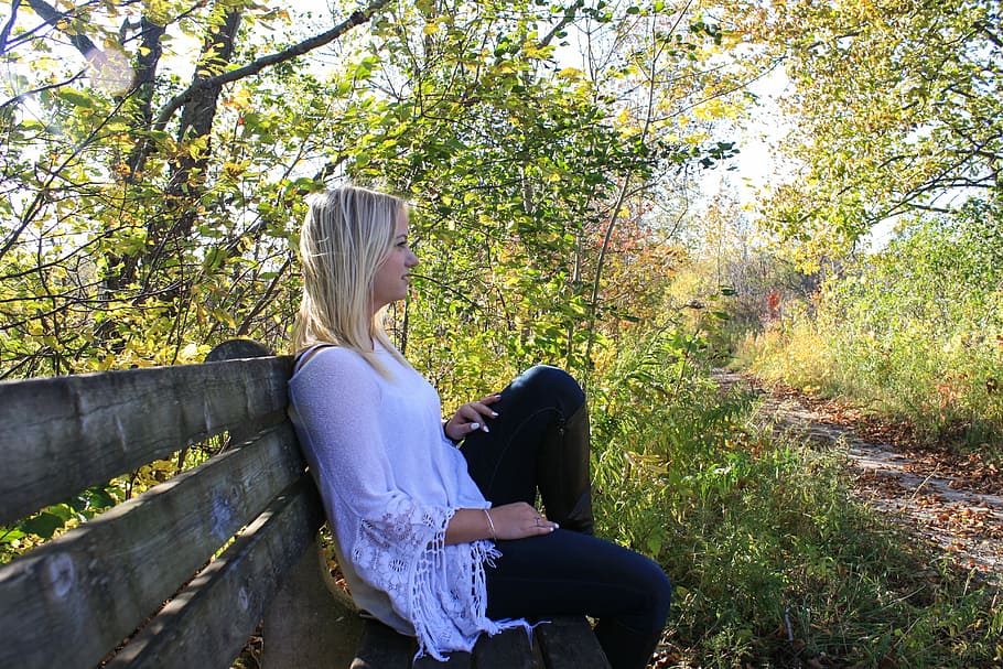 woman in white dress sits on bench chair near  tall trees at daytime HD wallpaper