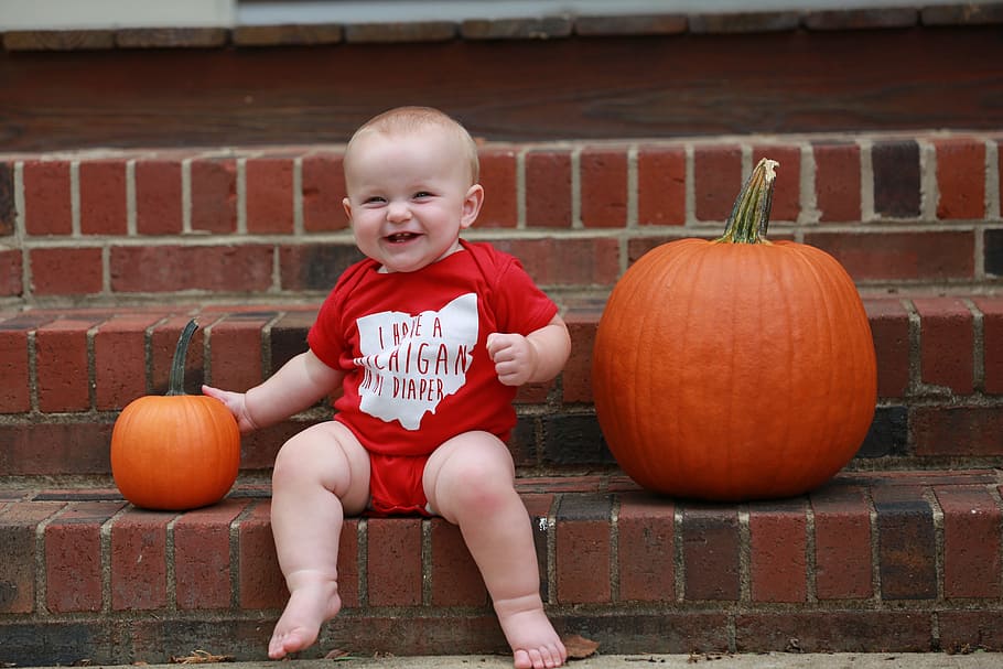 baby sitting beside two pumpkins while smiling, sports, ohio state
