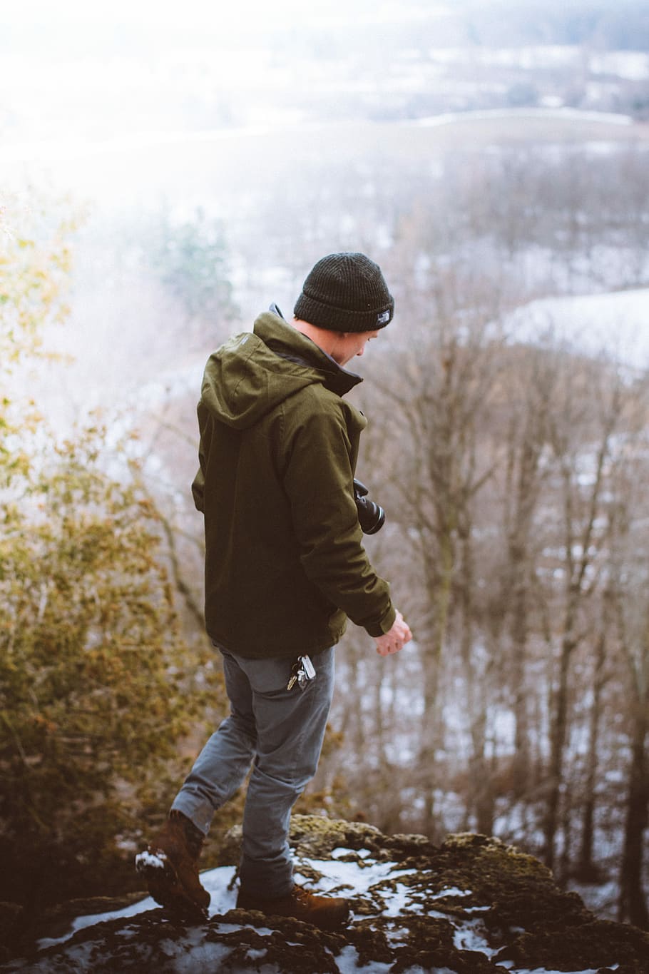 man standing on gray rock formation, man in black knit cap, green hooded jacket, blue denim jeans, and pair of brown boots standing on cliff during daytime, HD wallpaper