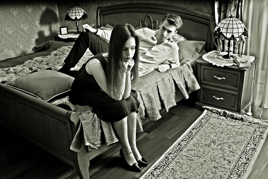 grayscale photo of woman sitting on bed near man lying on bed