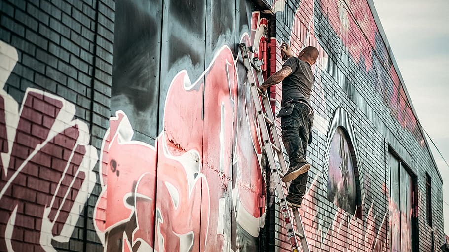 Man in Gray Shirt Standing on Gray Steel Ladder Painting Black White and Red Graffiti on Concrete Wall Outdoors HD wallpaper