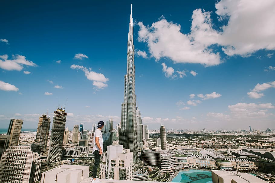 Burj Khalifa, Dubai during daytime, man standing alone on top of building looking at the city's tallest building during daytime