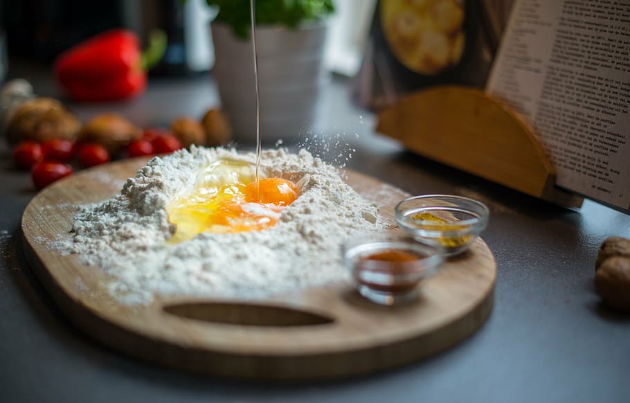 selective focus photography of raw egg surrounded by flour, breaking