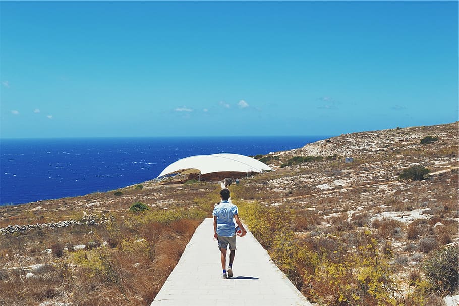 person in blue shirt walking on concrete pathway during day HD wallpaper