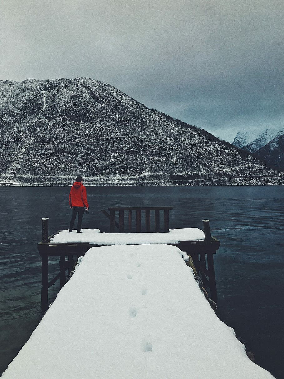 person standing on dock covered with snow looking at mountain across body of water, person standing on snow coated wooden dock at cloudy sky HD wallpaper