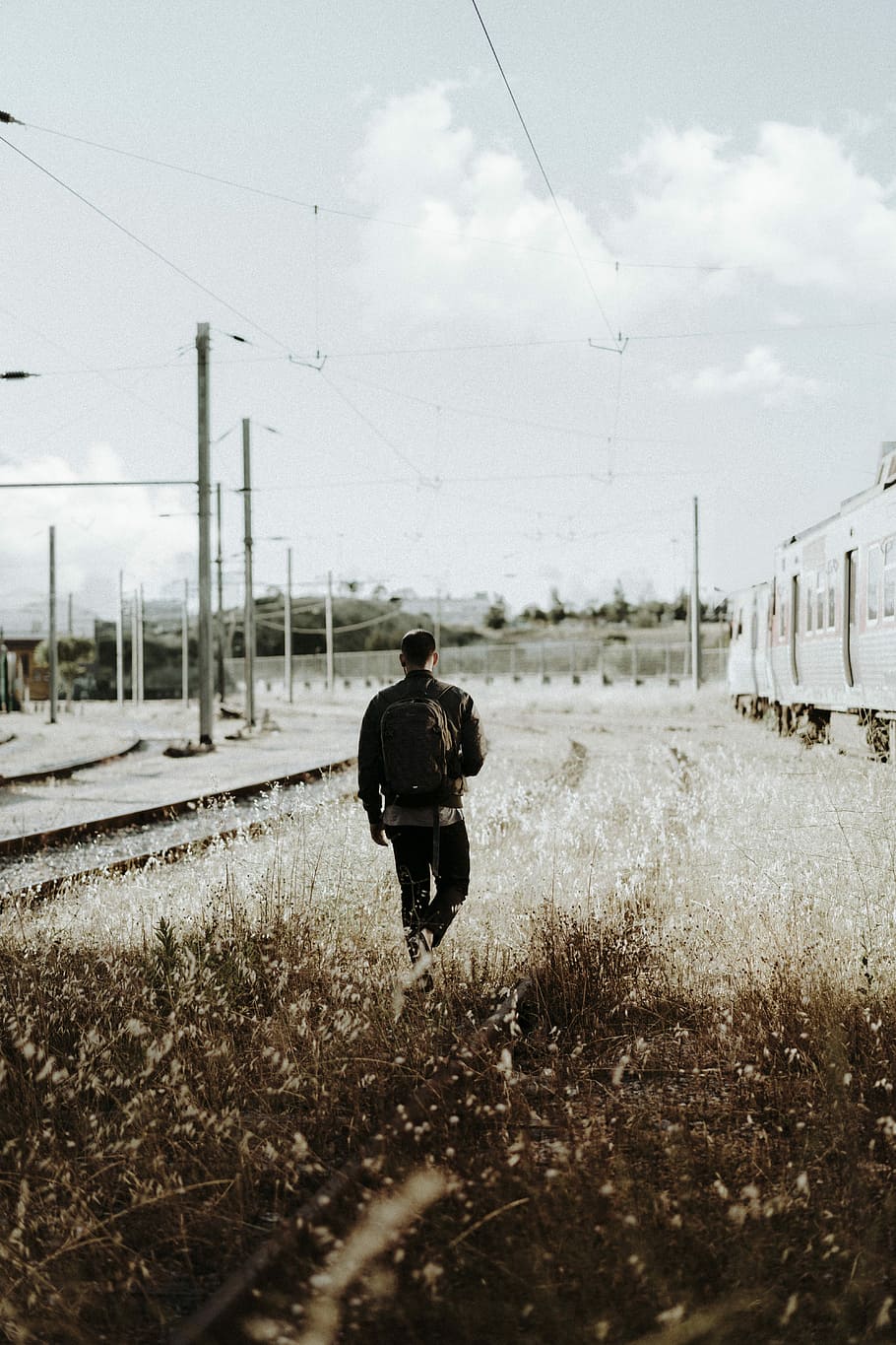 man walking into grass field during daytime, man in black backpack walking on grass near train HD wallpaper