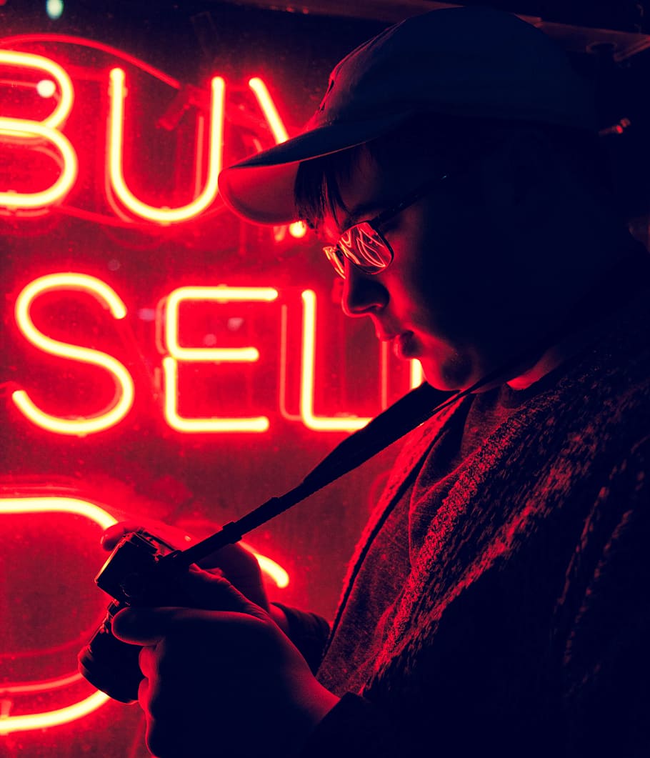 man standing in front of neon signage, man in cap standing beside buy and sell neon sign HD wallpaper